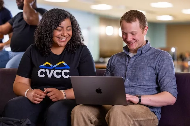 Two students seated on a coach looking at a laptop