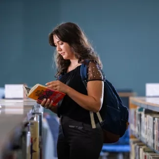 A woman standing between shelves of books holding a book