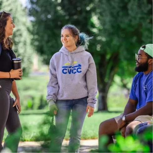 Three students outside. Two are standing and one is seated.