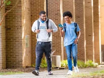 Two students wearing backpacks walking along a sidewalk